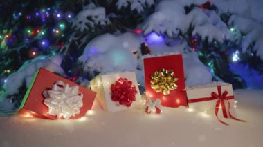 Tatil arkaplanındaki manzara kar yağışı. Birçok kırmızı ve beyaz hediye kutusu ve Noel süslemeleri güzel süslenmiş karlı Noel ağacının altında kış büyülü ormanlarında kar yağışlı gecelerde Bokeh ışıkları