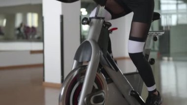 Güzel, atletik bir kadın sabit bisiklette egzersiz yapıyor. 30 'lu yaşlarda beyaz bir kadının yoğun bir şekilde at sürüşünü yakından izleyin. Yüksek kalite 4k görüntü