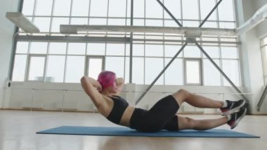 Aktif, atletik bir kız bir sürü penceresi olan parlak bir stüdyoda sırtını eğitiyor. Sportif, beyaz, pembe saçlı, temel mekik çeken bir kadın. Yüksek kalite 4k görüntü