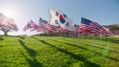 Güney Kore bayrağı rüzgarda dalgalanırken arka planda birçok Amerikan bayraklarıyla altın günbatımı saatinde güneş parlamasıyla birlikte. Ulusal Kore bayrağı bağımsızlığı, özgürlüğü ve turizm ortaklığını görselleştirdi
