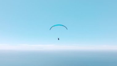 Paraglider açık mavi gökyüzünün arka planında süzülüyor. İnsansız hava aracının alt görüntüsü, ekstrem spor maceralarının sinematik havası, fotokopi alanı ve manzara arka planıyla yaz gökyüzünde bedava uçuş.