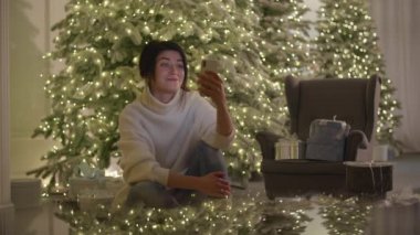 Aralık 2020. Esmer bayanın arka planında şık bir Noel aydınlatması olan bir video görüşmesi var. Beyaz kadın Xmas ağacının yanında oturuyor ve kameraya el sallıyor. Yüksek kalite 4k görüntü