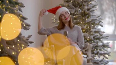 Yeni yıl partisinde şampanya içen bir kadın. Kız geleneksel Noel Baba şapkasını çıkarıp gülüyor. Yüksek kalite 4k görüntü