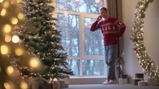 Man Praat Aan Telefoon Terwijl Hij Bij Het Raam Kerstboom — Stockvideo