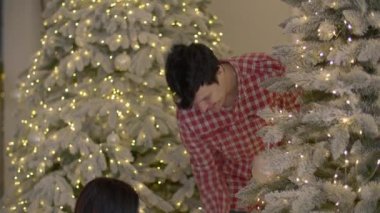 Mutlu aile Noel ağacını süslüyor. Ebeveynler ve kızları topları ve aydınlatmayı asarlar. Yüksek kalite 4k görüntü