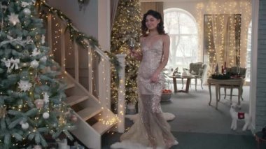 Büyüleyici elbiseli mutlu, şık kadın elinde bir bardak şampanyayla aşağıya iniyor. Gece kıyafetli esmer kadın Noel içeceği içer. Yüksek kalite 4k görüntü