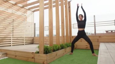 Siyah spor giyimli bayan sporcu ahşap terasta asana antrenmanı yapıyor. Kafkasyalı kadın sabahları dışarıda egzersiz yapıyor. Yüksek kalite 4k görüntü