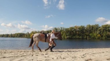 Genç, beyaz, yirmili yaşlarda bir jokey kumlu sahil boyunca bir atla geziyor. Bir hayvanı eğiterek boş zamanlardan zevk alan bir kadın. Yüksek kalite 4k görüntü
