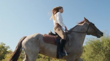 Neşeli, gülümseyen bir jokeyin açık mavi bir silueti olan at sırtında yakın plan çekimi. Genç, aktif bir bayan boş zamanlarını bir hayvanı eğiterek geçiriyor. Yüksek kalite 4k görüntü