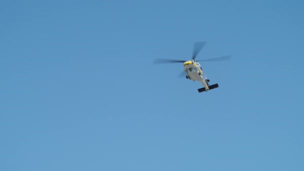澄んだ青い空を飛んで白い黄色のヘリコプターのスローモーションショット ロサンゼルス郊外での野火を区別した後 青い空を飛んで消防ヘリコプター シネマティックローアングルショットヘリ — ストック動画