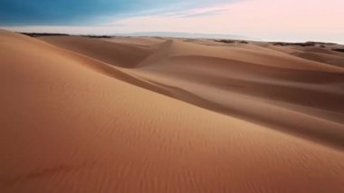 Vahşi doğada macera yolculuğu, destansı günbatımında hava görüntüleri. İnsansız hava aracı yüksek hızda alçaktan uçuyor. Manzaralı kum tepelerinin üstünde, günbatımında. Arka planda pembe bulutlar var.