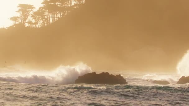 風光明媚な黄金の夕日の光と風の風で岩の海のコストで白いスプラッシュでクラッシュする強力な波のRedカメラで壮大なスローモーションショット 海岸の海水のエネルギーで背景をコピーします — ストック動画