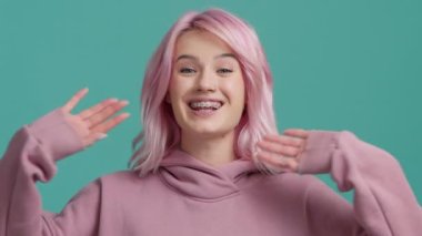 Genç mutlu hipster vlogger kızı pembe saçlı el sallayarak web kamerasına bakıyor izole edilmiş arka plan stüdyosunda kameraya konuşuyor. Yavaş çekim modeli sanal sohbet toplantısı için arıyor, sosyal uzaklık arkadaşı