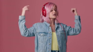 20 'li yaşlarda, rahat kot ceketli genç ve güzel bir kadın stüdyodaki pastel pembe arka planda yalnız poz veriyor. İnsanların yaşam tarzı konsepti. Dans etmek, eğlenmek, ifade etmek, el kol hareketi yapmak, ağır çekim.