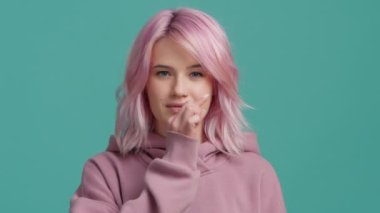 Yavaş çekim stüdyosu, pastel kapüşonlu pembe saçlı hipster mankeni olumlu gülümsüyor, kameraya bakıyor, fermuar çekiyor, ağzı kapalı sessizlik hareketi yapıyor, konuşmayı kes, 4K hakkında konuşmak istemiyorum.