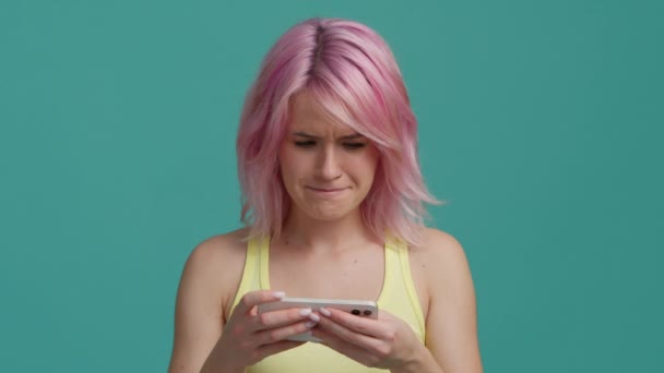 ピンクの髪をした若い十代のヒップスターの女の子は 友人や家族からの良いニュースで電子メールやテキストを受信します 教育やソーシャルメディアアプリについて スローモーション笑顔の顔に隔離された青の背景 — ストック動画