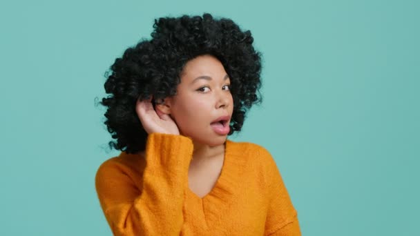 アフリカ系アメリカ人の女性は 耳の近くで話を聞き 疑問を表明し 情報を正しく聞くことができず 幼い頃に聴覚障害を抱えている 青の背景に屋内スタジオ — ストック動画