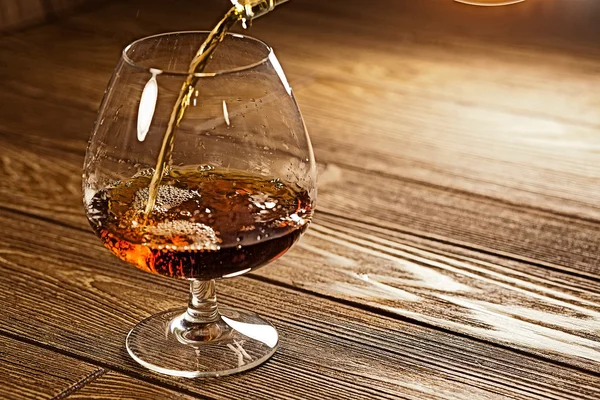 Vierta el brandy de una botella en un vaso sobre la mesa marrón — Foto de Stock