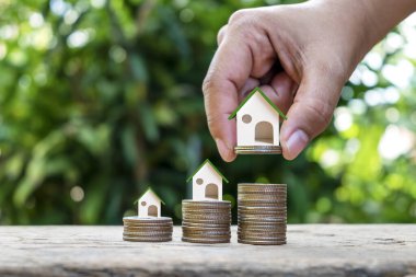 Bir yığın madeni para, emlak yatırım konsepti, ipotek ve ev inşa faiz oranları üzerinde model ev ve model ev tutan işadamı