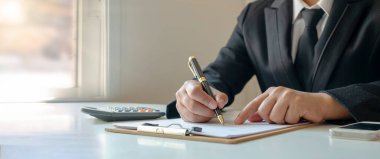 İş adamı finansal verileri analiz etmek için notlar alıyor ve mali belgelerin raporlarını kontrol ediyor. Çalışma kavramlarını, muhasebe belgelerini kontrol ediyor ve sözleşmeleri imzalıyor..