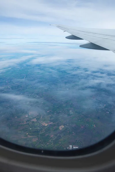 A view through the window of an airplane that sees the city, the fields, the sea and the clouds. See the flying wings that are flying in the sky