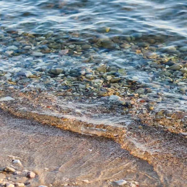 Hintergrund von Sand, Steinen und fließenden Wellen am Meeresstrand. Sommerferienkonzept — Stockfoto