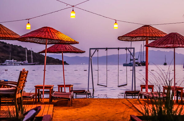 Summer vacation concept. Beach umbrellas, loungers and swings under red lanterns against backdrop of the sea at sunset