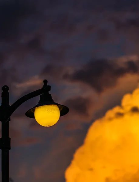 Background of a bright colorful sunset with orange clouds and a yellow street lamp — Stock Photo, Image