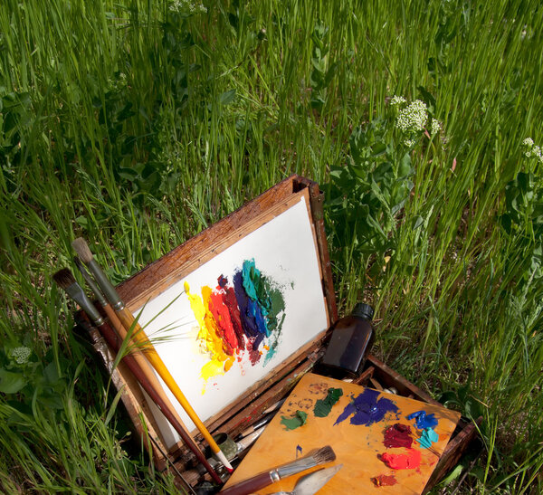 Painter's case on grass with palette, artistic tools and abstract painting