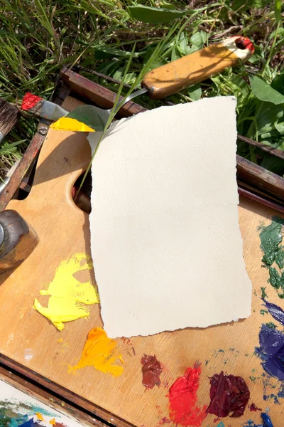 Textured paper on palette lying on painter case on the grass — Stock Photo, Image