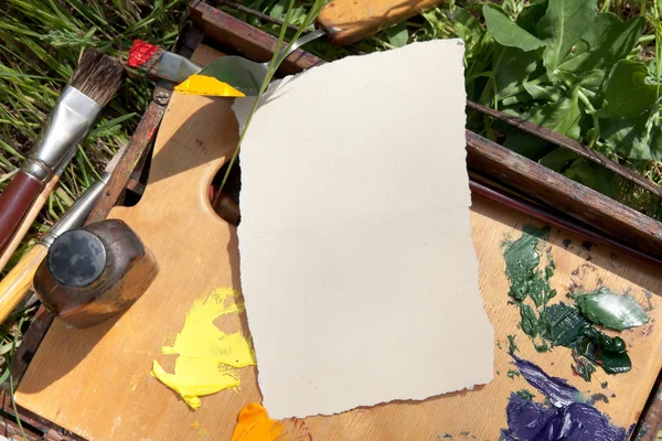 Textured paper on palette lying on painter case on the grass — Stock Photo, Image