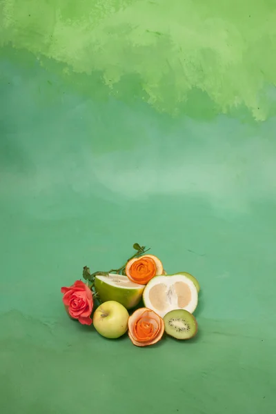 Roses and fruits on a green background — Stock Photo, Image
