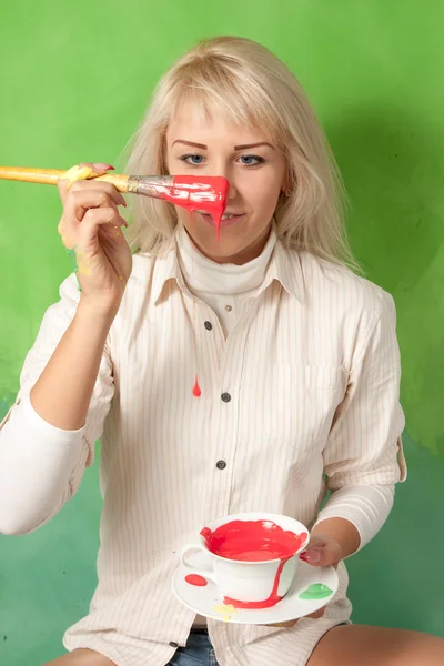 Jeune fille avec un pinceau et une tasse pleine de peinture rouge sur un fond vert — Photo