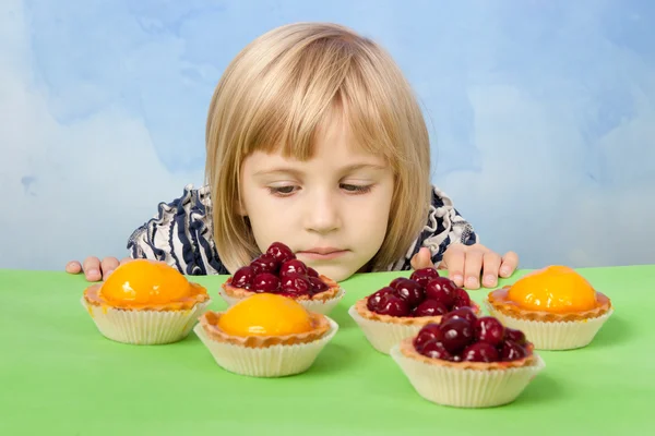 Kleines hübsches Mädchen blickt traurig auf Kirsch- und Pfirsichgelee-Torten — Stockfoto