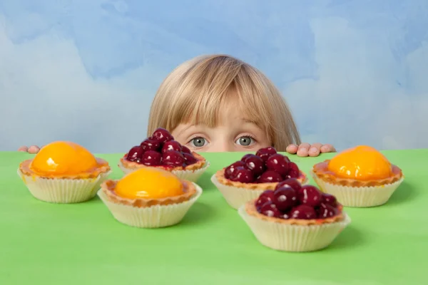 Szép kislány, feltörekvő mögül egy asztal, cseresznye, őszibarack és zselés torták — Stock Fotó