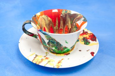 Beyaz fincan ve bir fincan tabağı ile mavi bir arka plan üzerinde boya lekeli