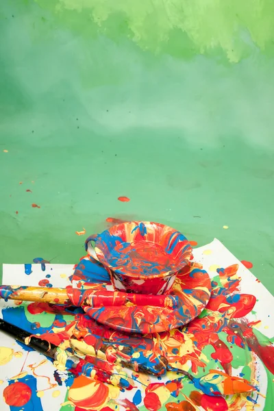 Tarjeta con taza de té y platillo lleno de pinturas brillantes con herramientas de pintura —  Fotos de Stock