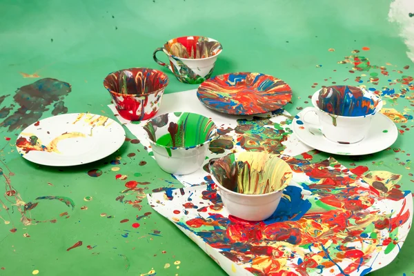 Cups with saucers all smudged with paint on a green background — Stock Photo, Image