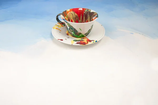 Карточка с белой чашкой и блюдцем, размазанная краской на белом и синем фоне — стоковое фото