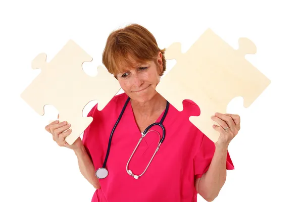 Krankenschwester mit verwirrtem Blick mit Puzzleteilen — Stockfoto