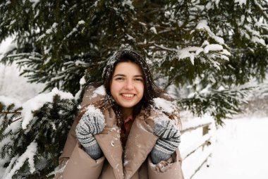 Güzel kız karda yürür. Kışın ormanda eğlenen genç bir kadın. Ormanda poz veren güzel esmer bir kadının açık hava portresi.