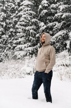 Kar yağarken sakallı yakışıklı adam yürür. Genç adam kış ormanında dikiliyor. Ormanda poz veren bir adamın açık hava portresi.