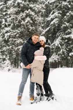 Mutlu aile kış ormanlarında eğleniyor. Anne, baba ve kızı karla oynuyor. Aile kavramı.