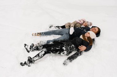 Mutlu aile kış ormanlarında eğleniyor. Anne, baba ve kızı yerde yatıp karla oynuyorlar. Aile kavramı. Birlikte vakit geçirmekten zevk alıyorum.