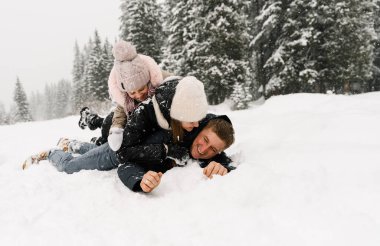 Mutlu aile kış ormanlarında eğleniyor. Anne, baba ve kızı yerde yatıp karla oynuyorlar. Aile kavramı. Birlikte vakit geçirmekten zevk alıyorum.