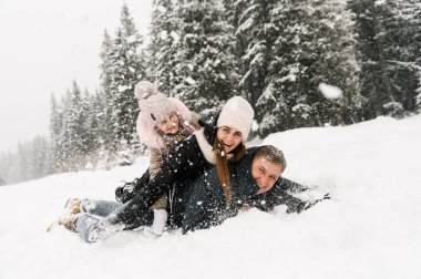 Mutlu aile kış ormanlarında eğleniyor. Anne, baba ve kızı yerde yatıp karla oynuyorlar. Aile kavramı. Birlikte vakit geçirmekten zevk alıyorum.