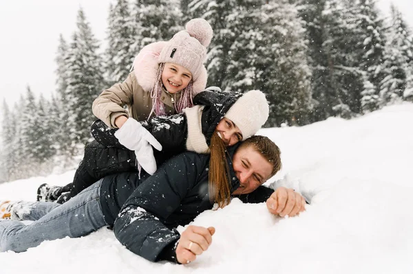 Mutlu aile kış ormanlarında eğleniyor. Anne, baba ve kızı yerde yatıp karla oynuyorlar. Aile kavramı. Birlikte vakit geçirmekten zevk alıyorum.