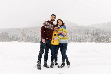 Mutlu aile kış ormanlarında eğlenir ve kameraya bakar. Anne, baba ve oğul karla oynuyor. Aile Noel konsepti. Birlikte vakit geçirmekten zevk alıyorum.