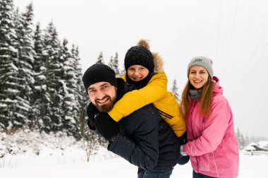 Mutlu aile kış ormanlarında eğlenir ve kameraya bakar. Anne, baba ve oğul karla oynuyor. Aile Noel konsepti. Birlikte vakit geçirmekten zevk alıyorum.
