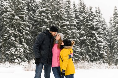 Mutlu aile kış ormanlarında eğlenir ve kameraya bakar. Anne, baba ve oğul karla oynuyor. Aile Noel konsepti. Birlikte vakit geçirmekten zevk alıyorum.